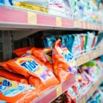 Prateleira de supermercado com diversas marcas de detergentes expostas.