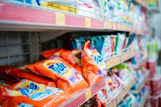 Prateleira de supermercado com diversas marcas de detergentes expostas.