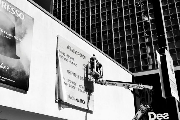 Trabalhador em uma plataforma elevatória ajusta um outdoor na fachada de um prédio.