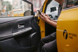 Motorista usa um celular sentado em um automóvel amarelo em uma área urbana.