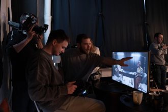 Equipe trabalha em um estúdio de gravação enquanto acompanha imagens em monitores.