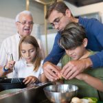 Três gerações de uma família preparam juntas uma refeição na cozinha.
