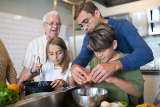 Três gerações de uma família preparam juntas uma refeição na cozinha.