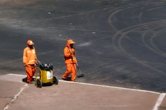 Dois trabalhadores da limpeza urbana usam uniformes laranja durante o trabalho em Brasília.