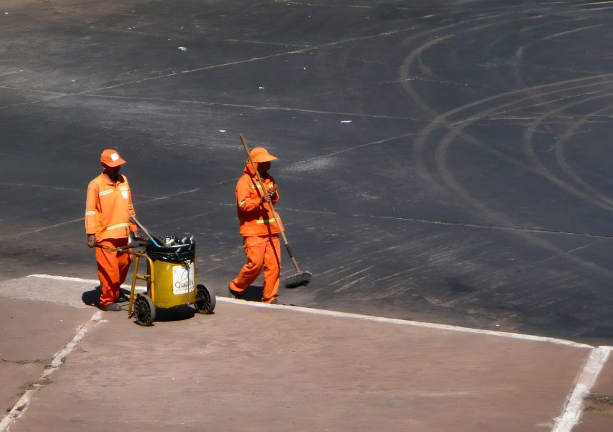 Dois trabalhadores da limpeza urbana usam uniformes laranja durante o trabalho em Brasília.